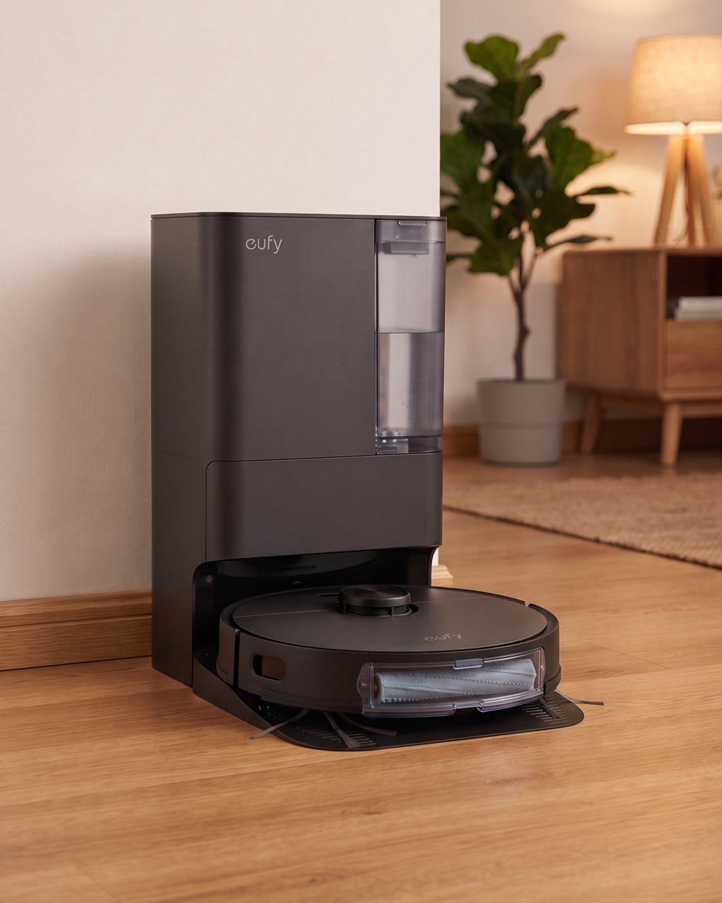 A eufy E25 robot vacuum docked in its tall charcoal station in a warm living room with oak floors.
