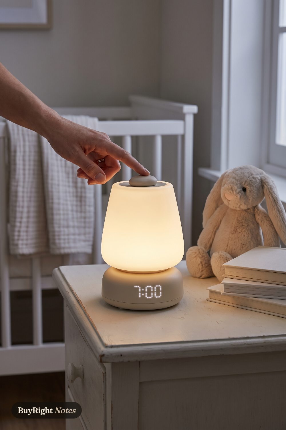 A parent's finger presses the button on top of a glowing Hatch Baby sound machine and night light showing 7:00, on a nursery dresser beside a plush bunny and a white crib.